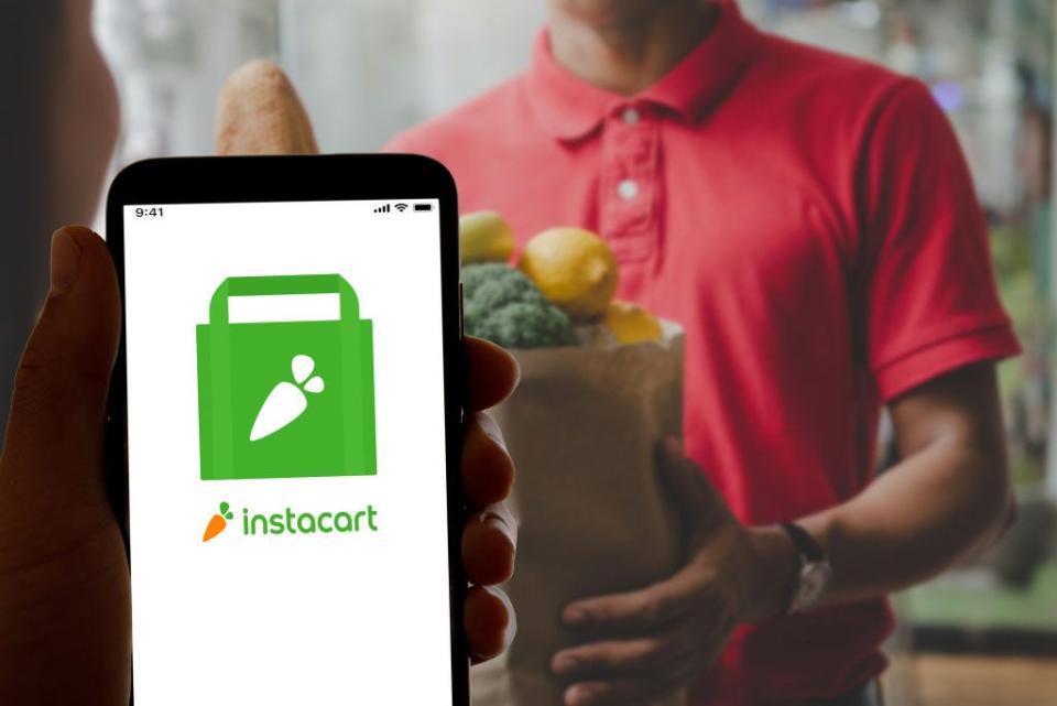 A phone showing instacart logo with a man holding a bag of groceries in the background