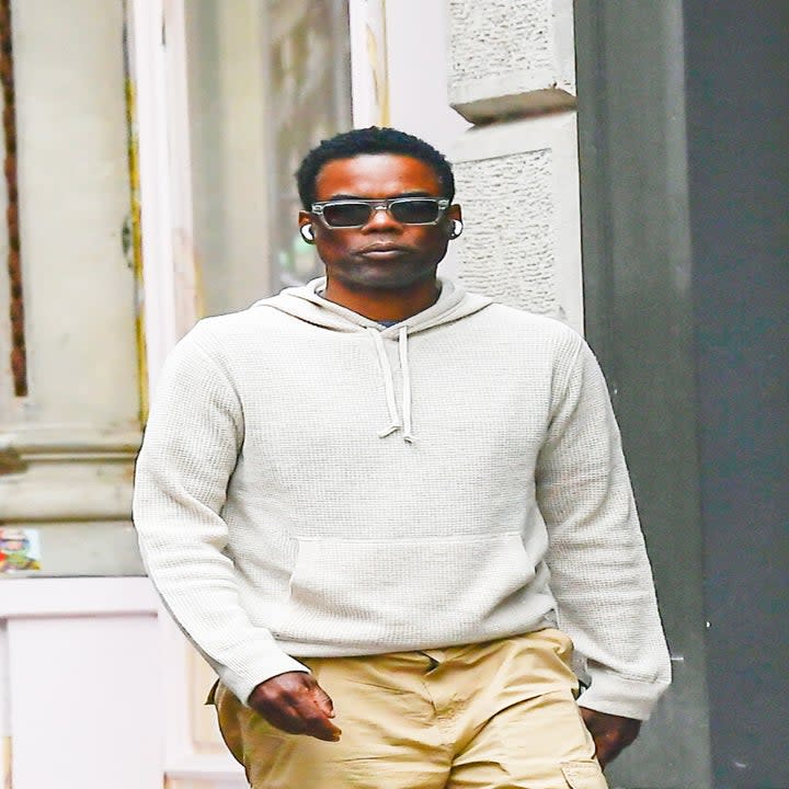 Chris Rock walks outside while wearing sunglasses and in-ear headphones