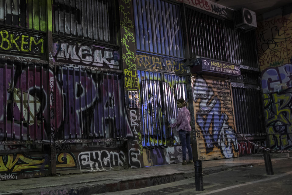 In this Thursday, July 25, 2019, a woman opens with her key the entrance of a building which is covered with graffiti in Psiri district, central Athens. Municipal authorities have repeatedly voiced determination to address the problem, with poor results so far. Anti-vandalism laws are rarely enforced and arresting perpetrators doesn't sit high among police priorities. (AP Photo/Petros Giannakouris)