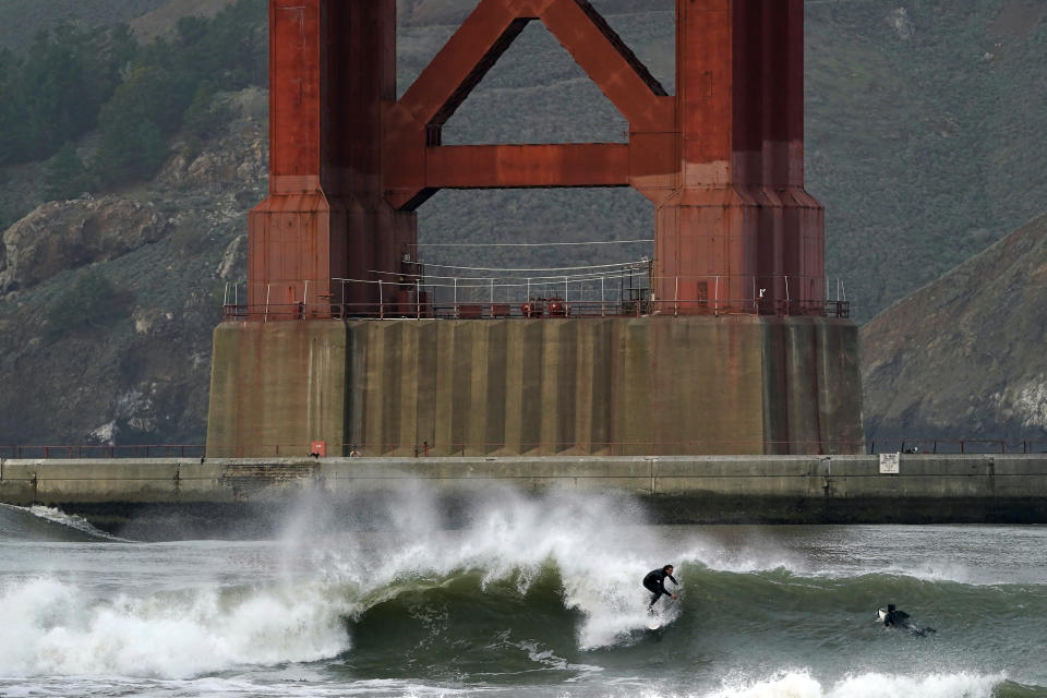 Surfers ride waves in front of a Golden Gate Bridge tower at Fort Point in San Francisco, Friday, Jan. 6, 2023. California weather calmed Friday but the lull was expected to be brief as more Pacific storms lined up to blast into the state, where successive powerful weather systems have knocked out power to thousands, battered the coastline, flooded streets, toppled trees and caused at least six deaths. (AP Photo/Jeff Chiu)