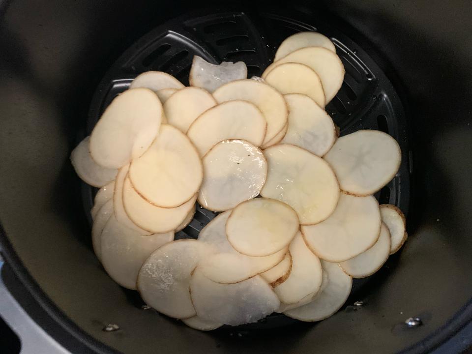 Slice potatoes laid out in the air fryer basket