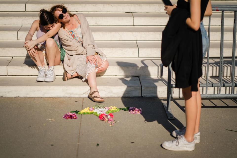 Two people leaning against each other as they sit on a white stairway next to a design made with flowers on the ground.