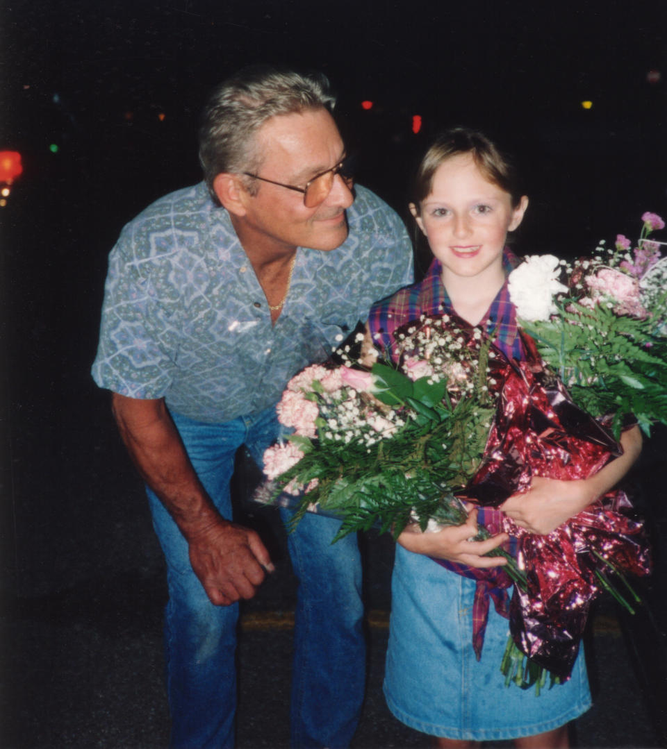 a dad looking down and smiling at his daughter who's carrying bouquets of flowers