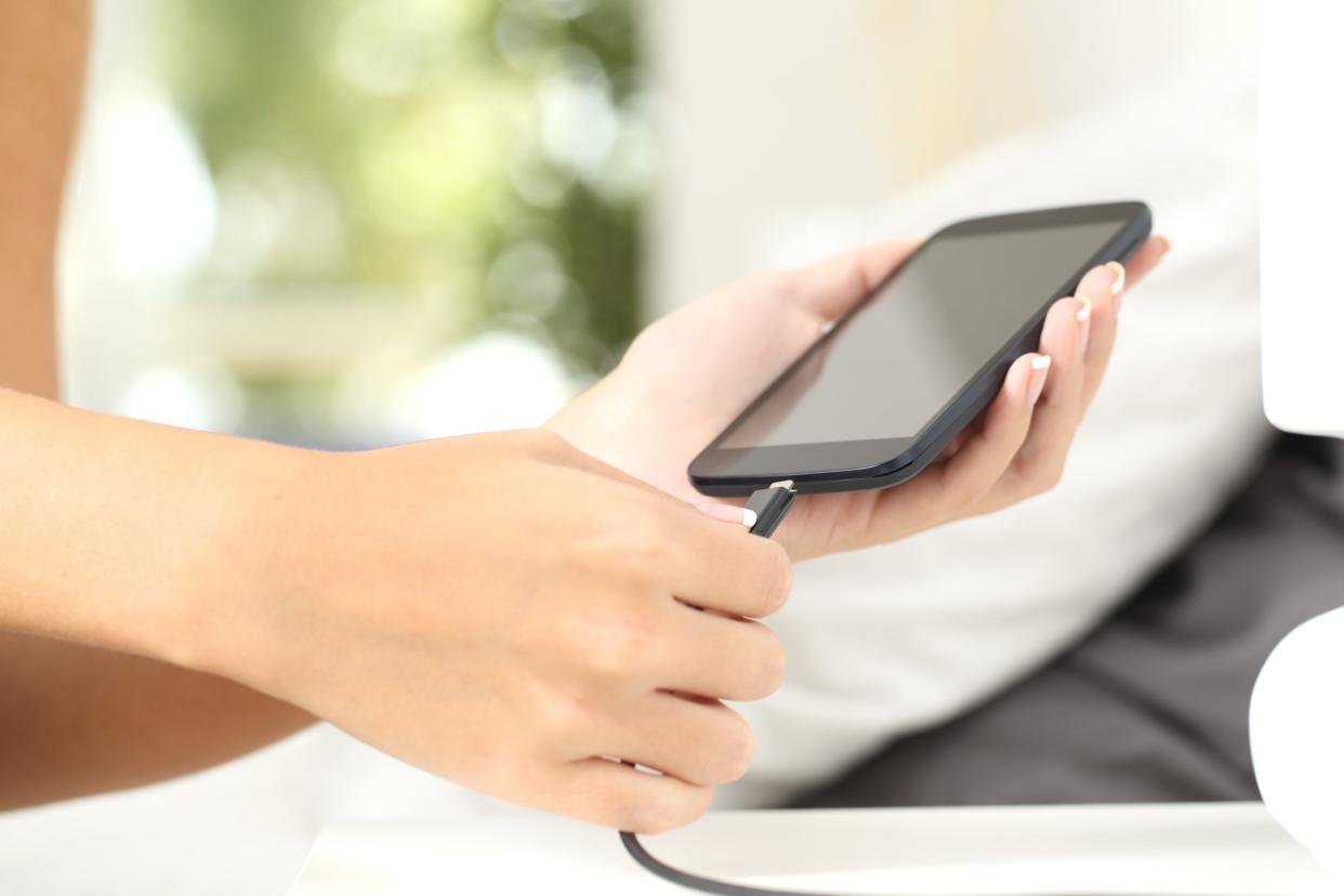 woman hands plugging a charger in a smart phone in the bedroom