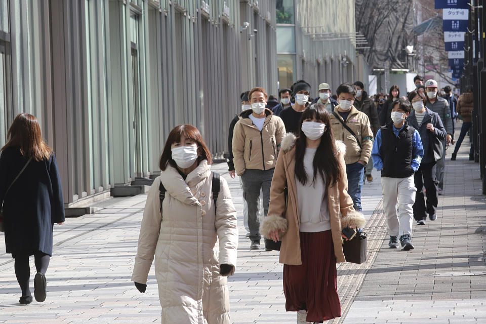 People wearing face masks to protect against the spread of the coronavirus walk along sidewalk in Tokyo, Tuesday, Feb. 2, 2021. (AP Photo/Koji Sasahara)