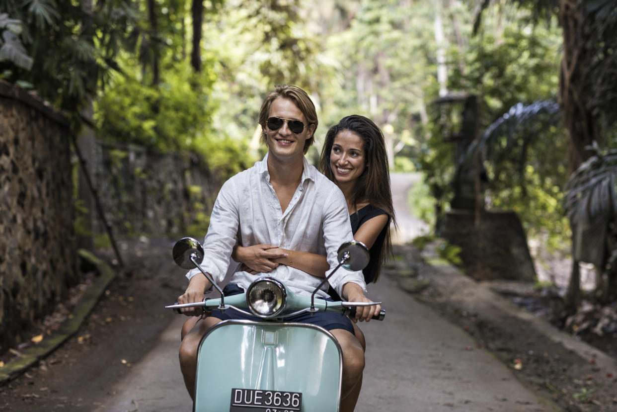 Asia, Indonesia, Bali, Young couple riding classic scooter along minor treelined road near Ubud.