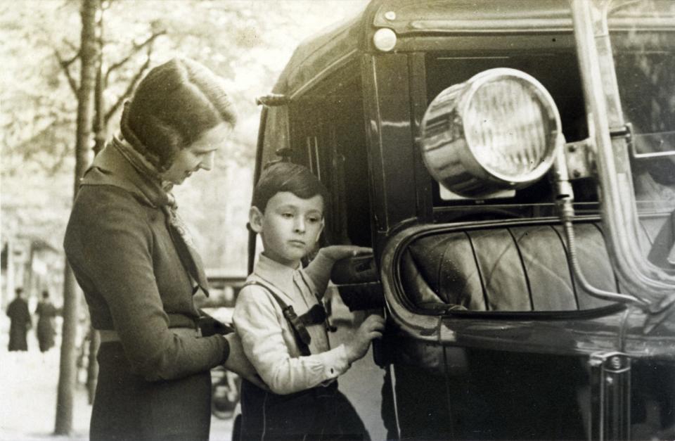 Young Mike Nichols and his mother, Brigitte Landauer, in a black and white photo of a street scene next to a car.