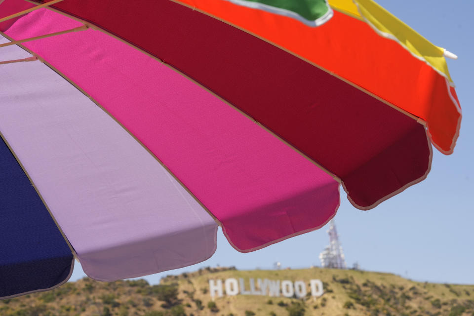 A rainbow umbrella stands with the Hollywood sign landmark seen in the background in Los Angeles, Wednesday, July 12, 2023. A heat wave that’s been scorching much of the U.S. Southwest is bringing triple digit temperatures and an increased risk of wildfires. (AP Photo/Damian Dovarganes)