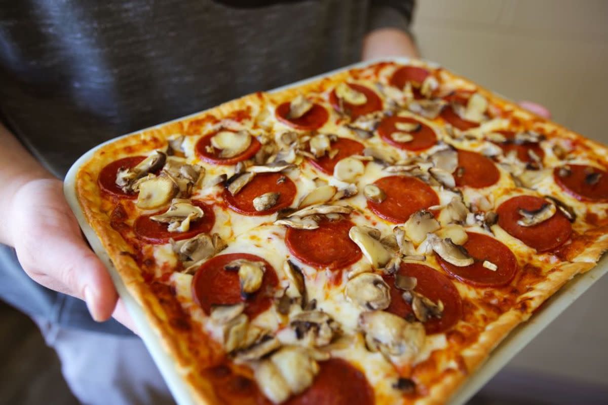 Closeup of rectangular pepperoni pizza in a white tray, Ledo Pizza, Washington, D.C., selective focus, mid-section of person holding the tray, jeans and grey shirt blurred