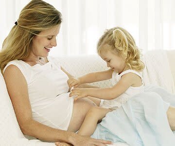 mother with daughter on lap touching pregnant belly