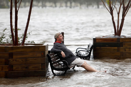 A man sits on a park bench in a flooded park as the Cape Fear River rises above its usual height in Wilmington, North Carolina, U.S., September 14, 2018. REUTERS/Jonathan Drake