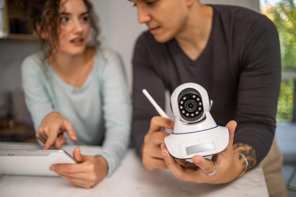 A young couple, a man and a woman, are setting up a security camera for home surveillance in their apartment