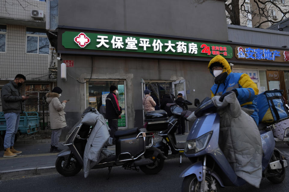 A delivery man passes by a line outside a pharmacy in Beijing, Friday, Dec. 9, 2022. China began implementing a more relaxed version of its strict "zero COVID" policy on Thursday amid steps to restore normal life, but also trepidation over a possible broader outbreak once controls are eased. (AP Photo/Ng Han Guan)