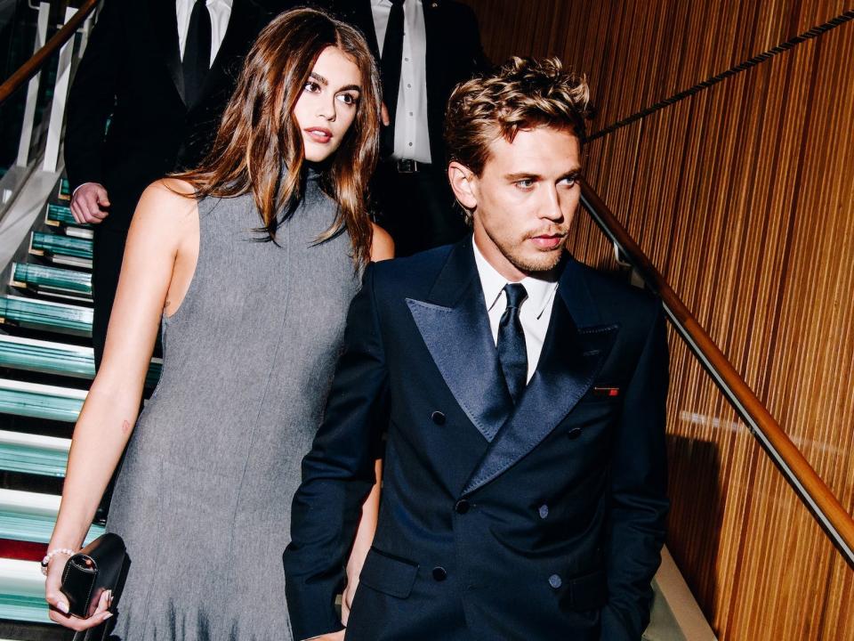 Kaia Gerber in a grey dress and Austin Butler in a black suit walking down stairs.