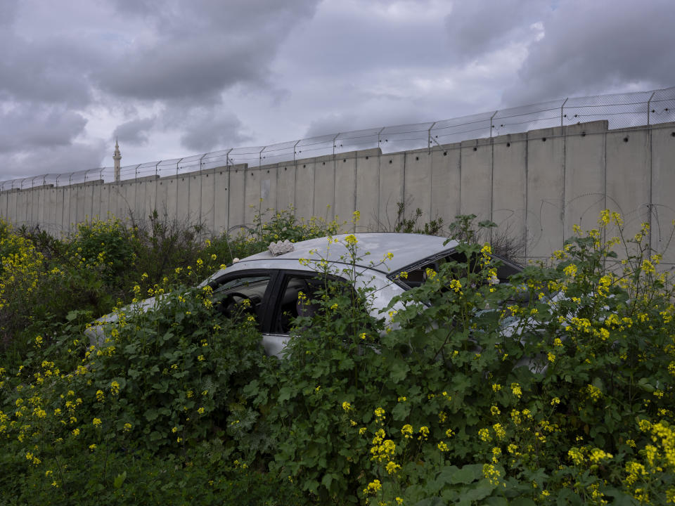 Bushes grow over an abandoned car next to section of the Israeli separation barrier in the northern Israeli Arab town of Baka Al-Gharbiye, separated from its neighbouring West Bank village of Nazlat Issa, Wednesday, March 9, 2022. Twenty years after Israel decided to built its controversial separation barrier amid a wave of Palestinian attacks, it remains in place, even as Israel encourages its own citizens to settle on both sides and admits tens of thousands of Palestinian laborers. (AP Photo/Oded Balilty)