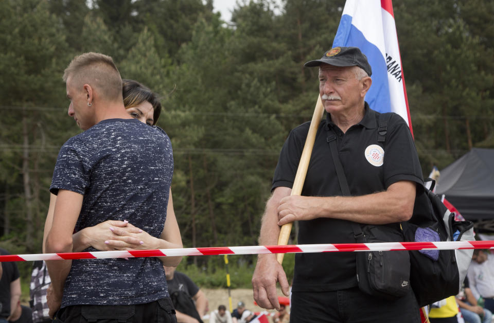 FILE - In this Saturday, May 12, 2018 file photo, a man holds Croatian flag as a couple embraces at the memorial site in Bleiburg, Austria. Thousands will gather in a field in southern Austria on Saturday, May 18, 2018, for an annual event to commemorate the massacre of tens of thousands mostly pro-Nazi soldiers known as Ustashas who fled to the village of Bleiburg in May 1945 amid a Yugoslav army offensive, only to be turned back by the British military and into the hands of revengeful antifascists. (AP Photo/Darko Bandic, File)