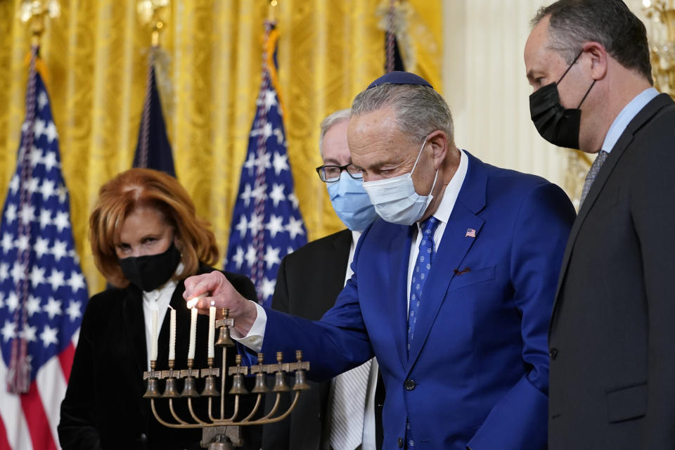 FILE - Senate Majority Leader Chuck Schumer of N.Y., second from right, lights the menorah in the East Room of the White House in Washington, during an event to celebrate Hanukkah, Dec. 1, 2021. Others watching are, from left, Jewish community leader Susan Stern, Dr. Rabbi Aaron Glatt, and second gentleman Doug Emhoff. (AP Photo/Susan Walsh, File)