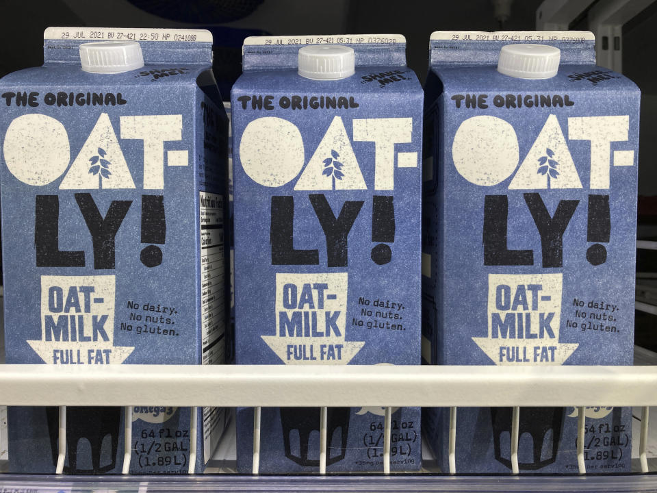 Three Oatly oat milk containers on a grocery store shelf.