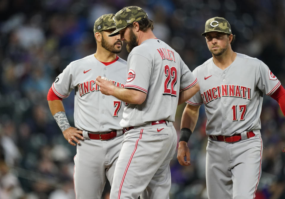 Cincinnati Reds starting pitcher Wade Miley, front, waits to be pulled from the mound as third baseman Eugenio Suarez, back left, and shortstop Kyle Farmer look on in the fourth inning of a baseball game against the Colorado Rockies, Friday, May 14, 2021, in Denver. (AP Photo/David Zalubowski)