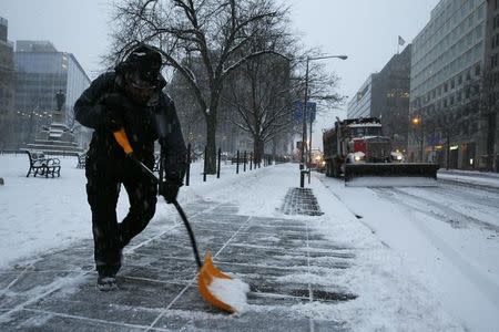 A man shovels snow from a sidewalk as a plow truck clears a street after a winter storm arrived in Washington January 22, 2016. REUTERS/Jonathan Ernst