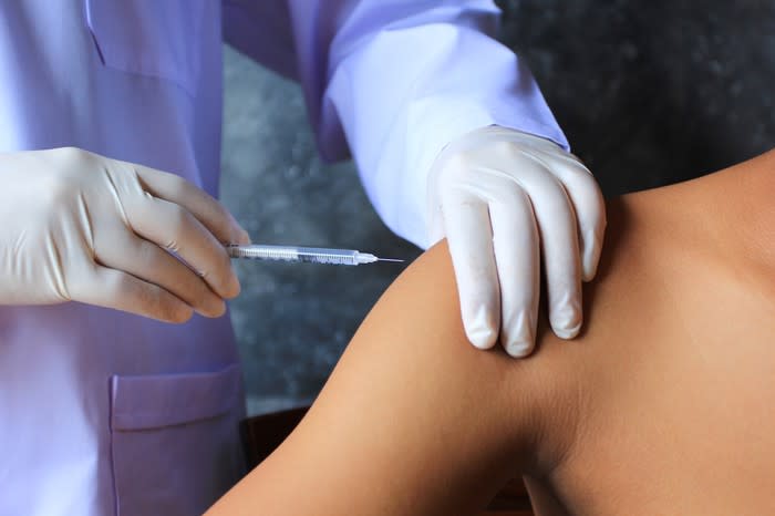 Gloved hands giving a shot into the shoulder of a patient