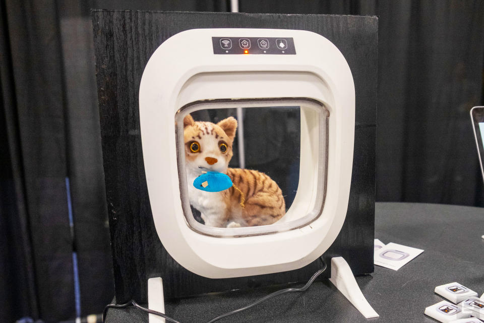 Una puerta para gatos Flappie blanca instalada en un cuadrado de madera negra con un gato y un ratón de peluche detrás en exhibición en CES 2024.