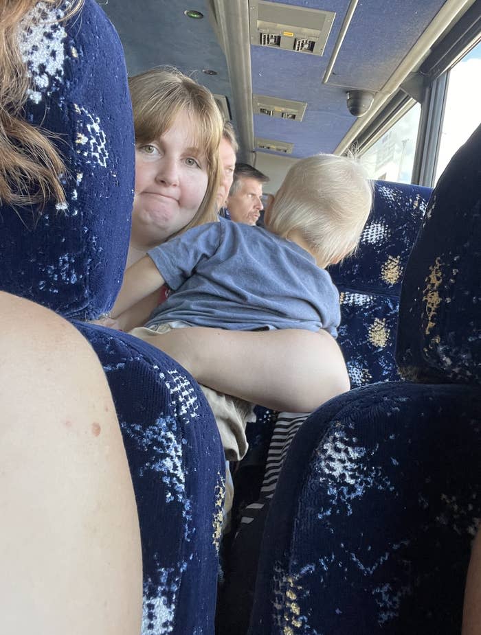 A woman holds a child on her lap while sitting on a bus. Several passengers are seated around them