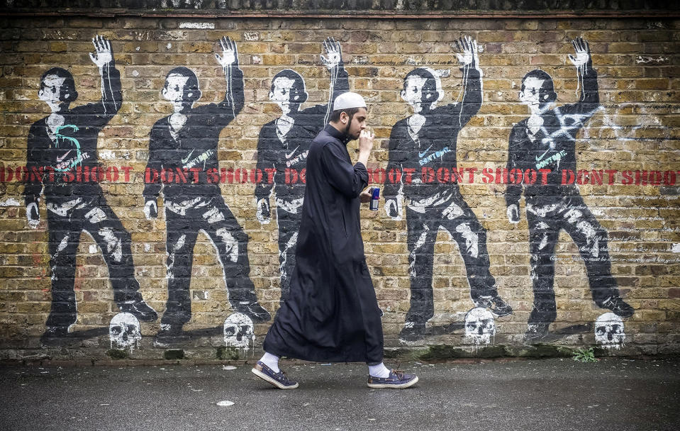 A young Muslim man walks past a Black Lives Matter-style mural in London
