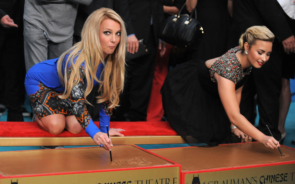 Judges Britney Spears, left, and Demi Lovato sign their names during a handprint ceremony at "The X Factor" season two premiere at Grauman's Chinese Theatre on Tuesday, Sept. 11, 2012, in Los Angeles. (Photo by Jordan Strauss/Invision/AP)