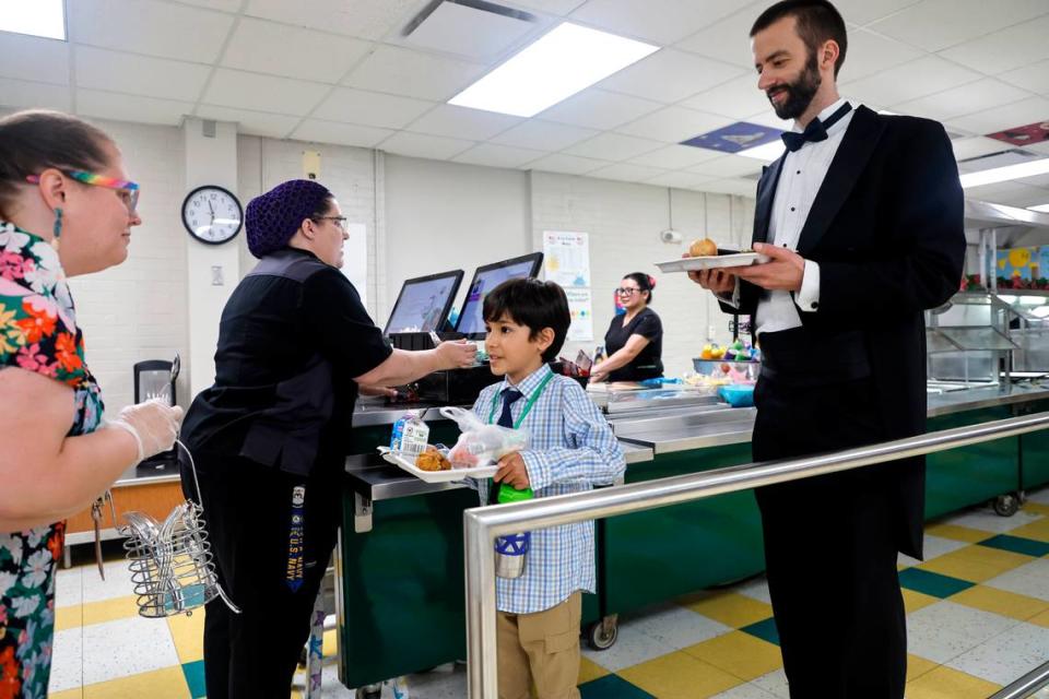 Combs Elementary School’s Tiffany Webb asks second grader Esteban Sepuldeva if he would like a fork with his lunch during the Silver Tray Luncheon at Combs Elementary School in Raleigh, N.C., Thursday, May 16, 2024. School counselor Sam Woodrum, right, waits. At the Silver Tray Luncheon there is fancy silverware, cafeteria tables have tablecloths and centerpieces as the Enloe High School orchestra plays music to provide a fine dining experience. The dining experience was the culmination of a year-long effort to teach Combs’ students about the value of social etiquette and good manners.