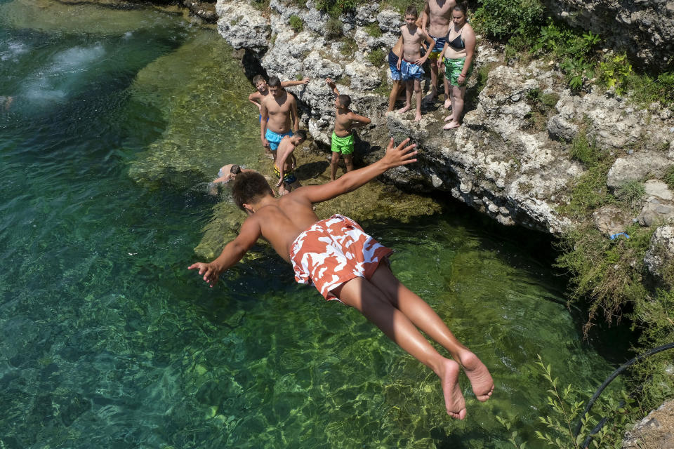 A boy dives into the Cijevna river near Montenegro's capital Podgorica, as temperatures soared to 36 degrees Celsius (96.8 Fahrenheit) on Thursday, July 11, 2024. Weather alerts, forest fires, melting pavement in cities: A sizzling heat wave has sent temperatures in parts of central and southern Europe soaring toward 40 degrees Celsius (104 Fahrenheit) in some places. (AP Photo/Risto Bozovic)