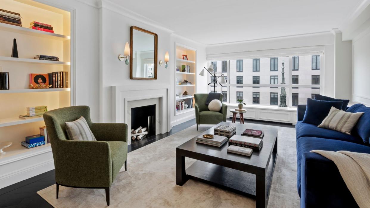  living room in white with blue sofa, 2 green armchairs, fireplace and bookshelves left and right of fireplace  