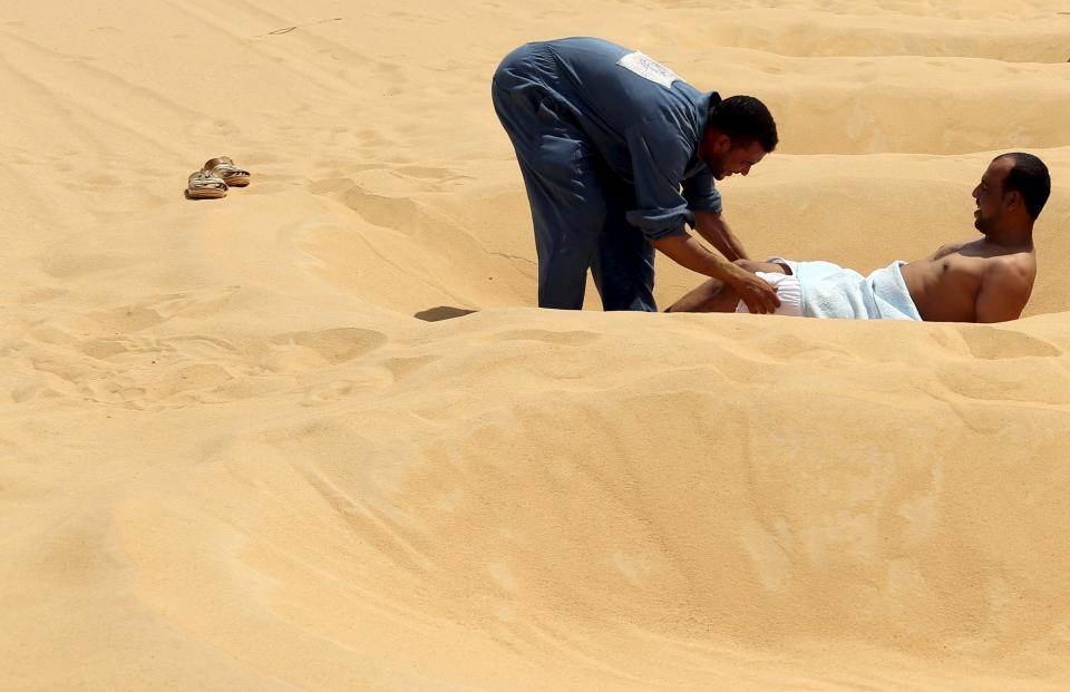 A worker helps a patient take off his clothes before he's buried in the sand in Siwa, Egypt, August 11, 2015.(REUTERS/Asmaa Waguih)