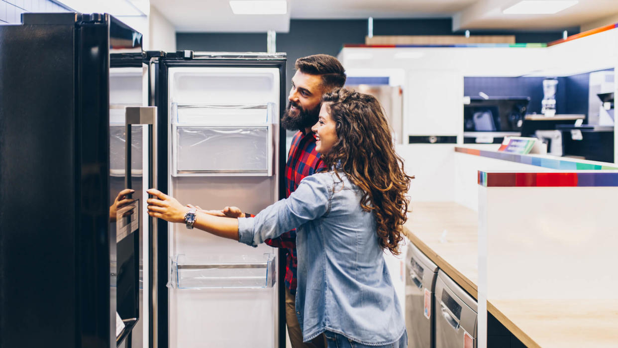 Young couple, satisfied customers choosing fridges in appliances store.