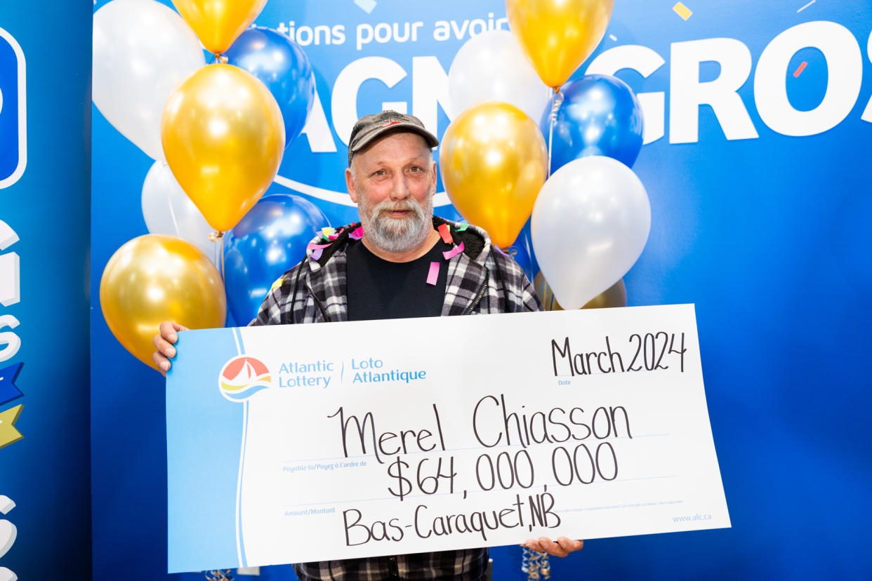 Man holding a $64 million cheque after winning the Gold Ball jackpot