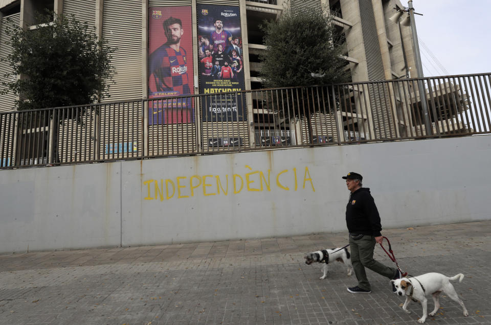 A man with two dogs walks past a graffiti reading "Independence" outside the Camp Nou stadium ahead of a Spanish La Liga soccer match between Barcelona and Real Madrid in Barcelona, Spain, Wednesday, Dec. 18, 2019. Thousands of Catalan separatists are planning to protest around and inside Barcelona's Camp Nou Stadium during Wednesday's match against fierce rival Real Madrid. (AP Photo/Bernat Armangue)