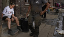 Resident Eric Mouque, center, walks by his wife Cindy Mouque as they take a rest after cleaning up their flood damaged home in the La Brouck neighborhood of Trooz, Belgium, Tuesday, July 27, 2021. The Mouque's are among hundreds of survivors in the small town of Trooz experiencing symptoms of post-traumatic stress disorder, depression and anxiety. (AP Photo/Virginia Mayo)