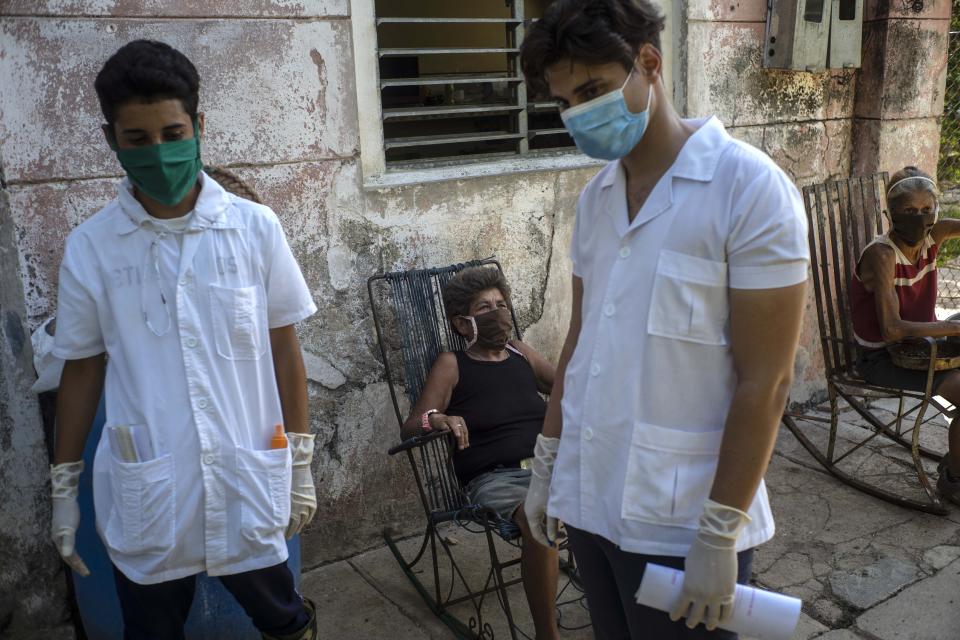 Medical students Hector Manuel Batista, left, and Ricardo Delgado, interview an elderly resident as two others sit in rockers wearing protective face mask as a measure to curb the spread of the new coronavirus, during their search in the countryside for people infected with COVID-19, in San Jose de las Lajas, Cuba, Thursday, April 30, 2020. (AP Photo/Ramon Espinosa)