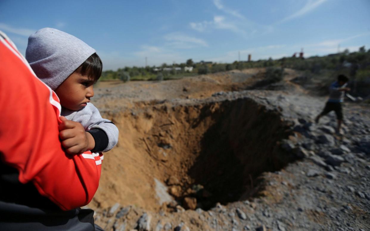 A Palestinian boy is carried as he looks at the scene of an Israeli air strike - REUTERS