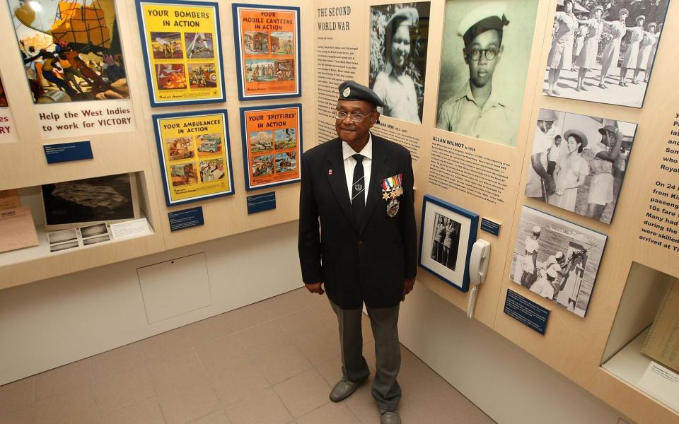 Wilmot in 2008 beside a photo of him as a boy at the exhibition From War to Windrush at the Imperial War Museum in London - Cate Gillon