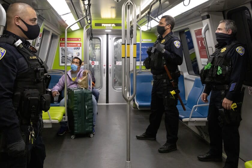 FILE - San Francisco Bay Area Rapid Transit police officers Nick Luzano, left, Eric Kelly, center, and Eric Hofstein, right, wear masks while patrolling a Richmond bound train from Powell Street Station BART platform in San Francisco, Calif., on Nov. 20, 2020. The BART board of directors decided, Thursday, April 28, 2022, to temporarily restore a mask mandate for riders on the rail system a week after it was dropped. The new mandate is effective until July 18, unless extended. (Jessica Christian/San Francisco Chronicle via AP, File)