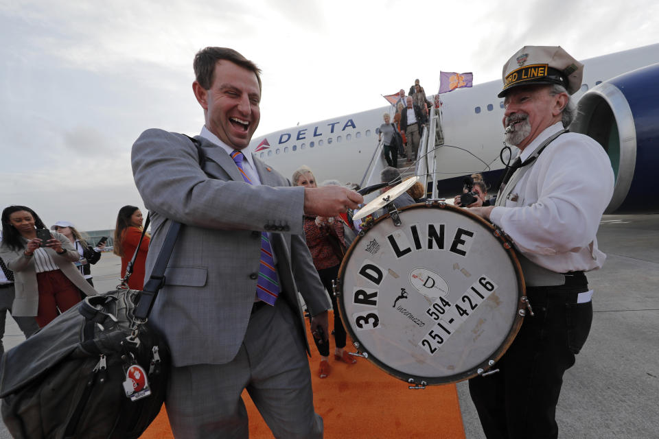 Clemson coach Dabo Swinney plays the cymbal on the drum of a member of the 3rd Line Brass Band as he arrives with the team for the NCAA College Football Playoff title game in New Orleans, Friday, Jan. 10, 2020. Clemson is scheduled to play LSU on Monday. (AP Photo/Gerald Herbert)