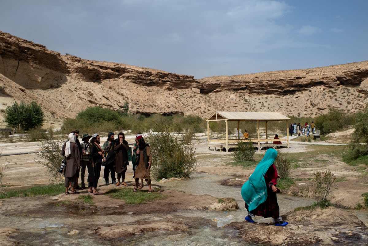 An Afghan woman walks past Taliban members at Band-e Amir National Park, a popular weekend destination, in Band-e Amir, central Afghanistan (Getty)