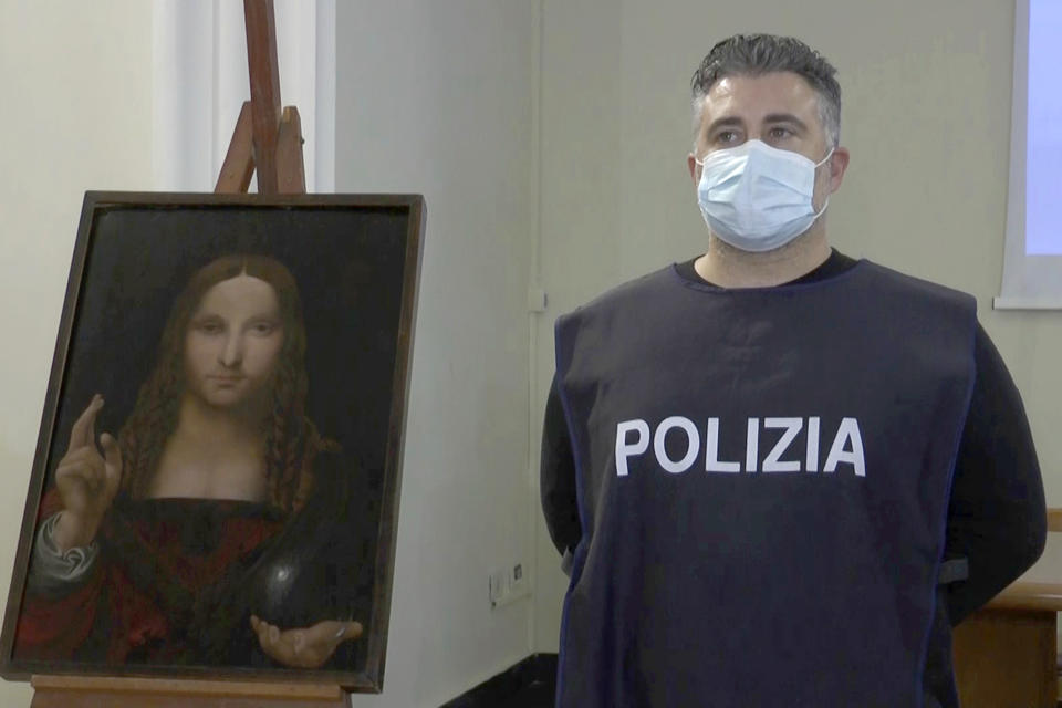 In this image taken from a video, a police officer poses by a copy of the “Salvator Mundi” (Savior of the World) by Leonardo da Vinci, in Naples, Italy, Wednesday, Jan. 20, 2021. Italian police have recovered a copy of Leonardo da Vinci’s 16th century “Salvator Mundi” painting of Jesus Christ that was stolen from a Naples church without the priests even realizing it was gone. The discovery was made over the weekend when Naples police working on a bigger operation found the painting hidden in an apartment. Police chief Alfredo Fabbrocini said the owner offered a “less than credible” explanation that he had “casually” bought it at a small market. (AP Photo/Sicomunicazione)