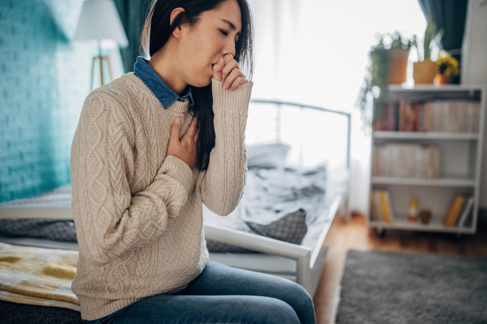 Person sitting on a couch, coughing or clearing throat, in a casual indoor setting