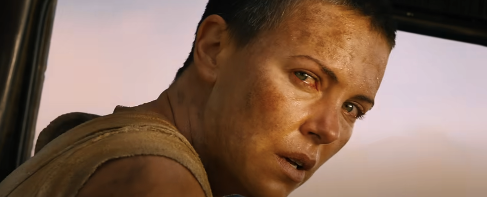 Furiosa, a character from Mad Max, looks intently through a vehicle's window