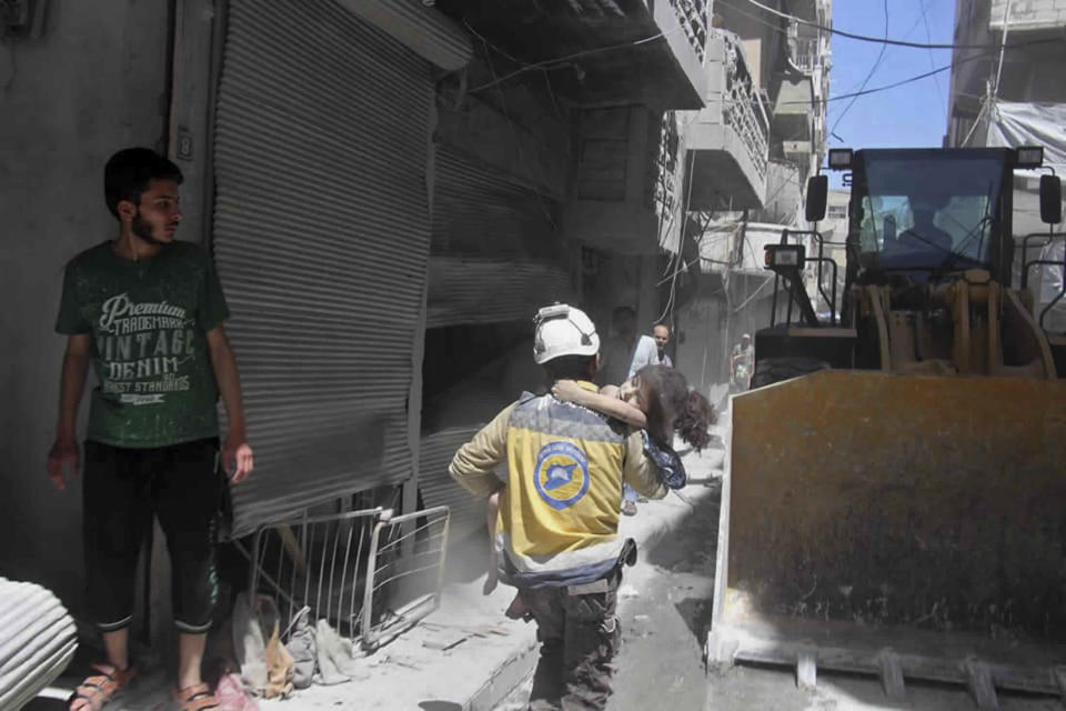 This photo provided by the Syrian Civil Defense White Helmets, which has been authenticated based on its contents and other AP reporting, shows a civil defense worker carrying a child after an airstrike by the Syrian government forces, in the town of Ariha, in the northwestern province of Idlib, Syria, Monday, May 27, 2019. Syria's White Helmets say at least six people were killed and 10 remain under rubble following government air raids on a town in the rebel's last stronghold. (Syrian Civil Defense White Helmets via AP)