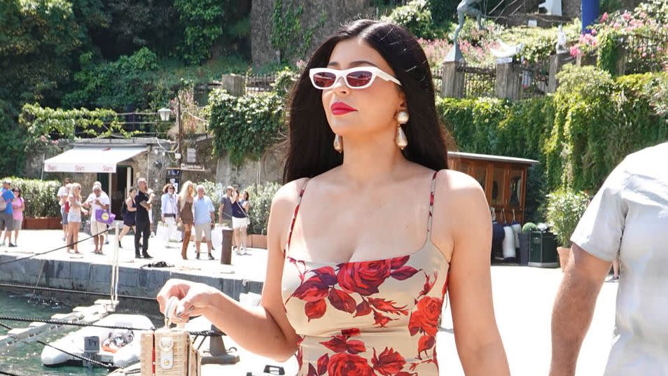 <p>matches her lips to her floral Dolce & Gabbana dress, teamed with a straw bag, lucite sandals, white sunnies and oversize drop pearl earrings for a day of celebrating on Saturday. </p>