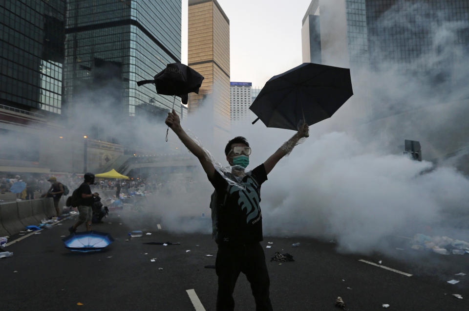 A protester (C) raises his umbrellas in front of tear gas which was fired by riot police to disperse protesters blocking the main street to the financial Central district outside the government headquarters in Hong Kong, September 28, 2014. Hong Kong police used tear gas for the first time on Sunday to disperse pro-democracy protests and baton-charged the crowd blocking a key road in the government district after Hong Kong and Chinese officials warned against illegal demonstrations. REUTERS/Tyrone Siu (CHINA - Tags: CIVIL UNREST POLITICS TPX IMAGES OF THE DAY)