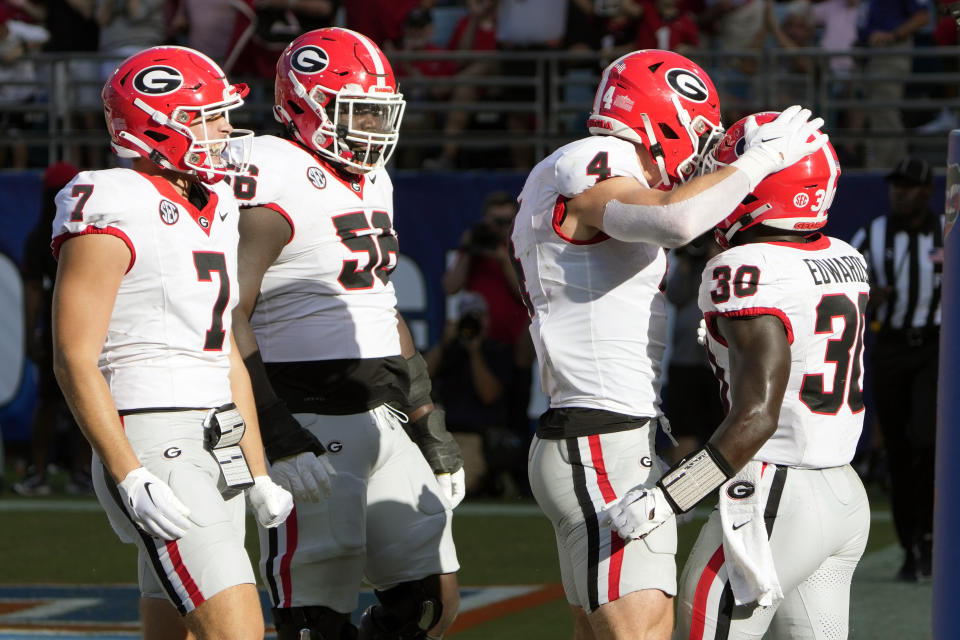 Georgia players, from left, tight end Lawson Luckie (7), offensive lineman Micah Morris (56) and tight end Oscar Delp (4) celebrate with running back Daijun Edwards (30) after he scored a touchdown on a 2-yard run during the first half of an NCAA college football game against Florida, Saturday, Oct. 28, 2023, in Jacksonville, Fla. (AP Photo/John Raoux)